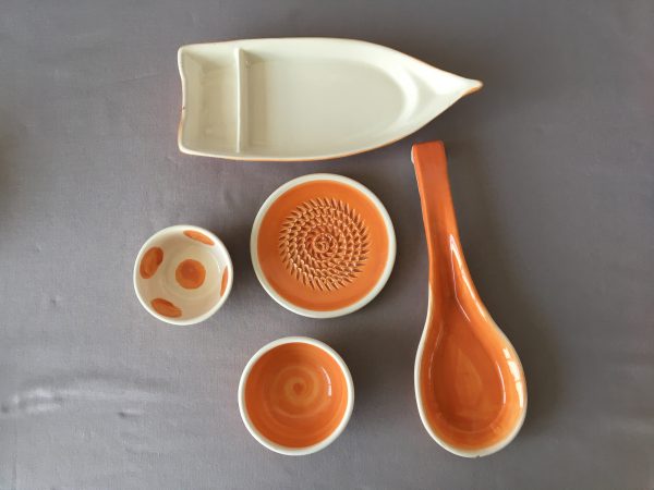 Keramikartikel in orange Schiffchen, Löffel, Reibe und Teller, passend zur Keramikschale